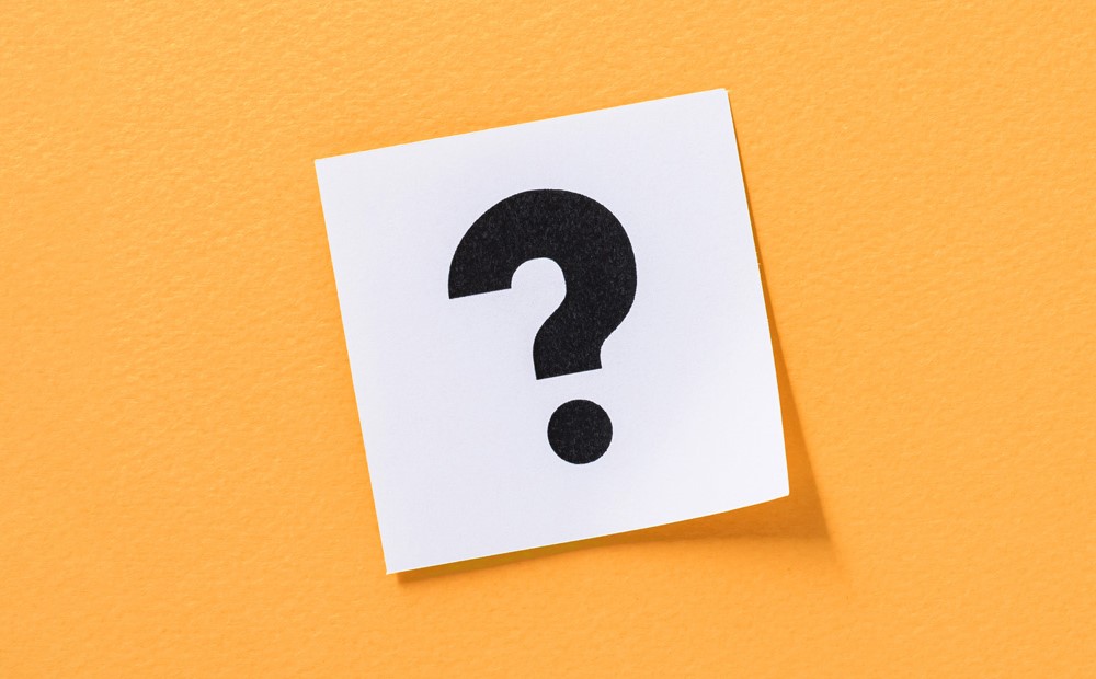 A question mark on a white sticky note against an orange background