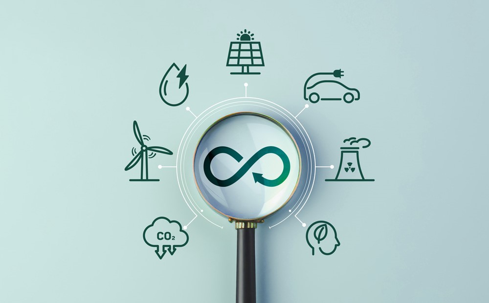 A magnifying glass looking at an infinite symbol with several sustainability icons surrounding it against a teal background.